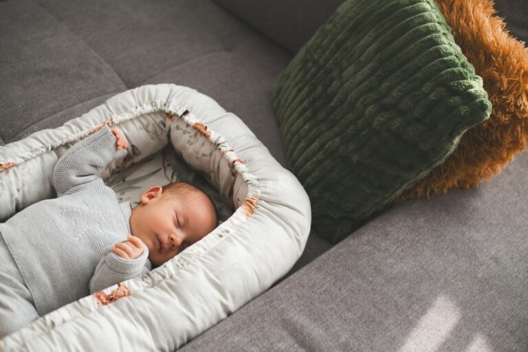 Bébé couché dans un réducteur de lit (babynest) aux bords rembourrés, posé sur un canapé